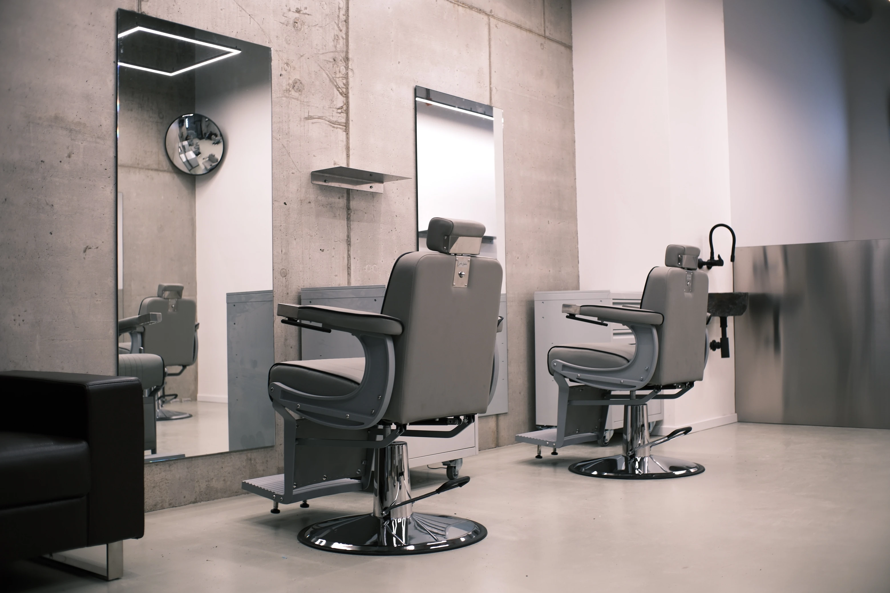 Dvě barberská křesla před zrcadly na betonové stěně