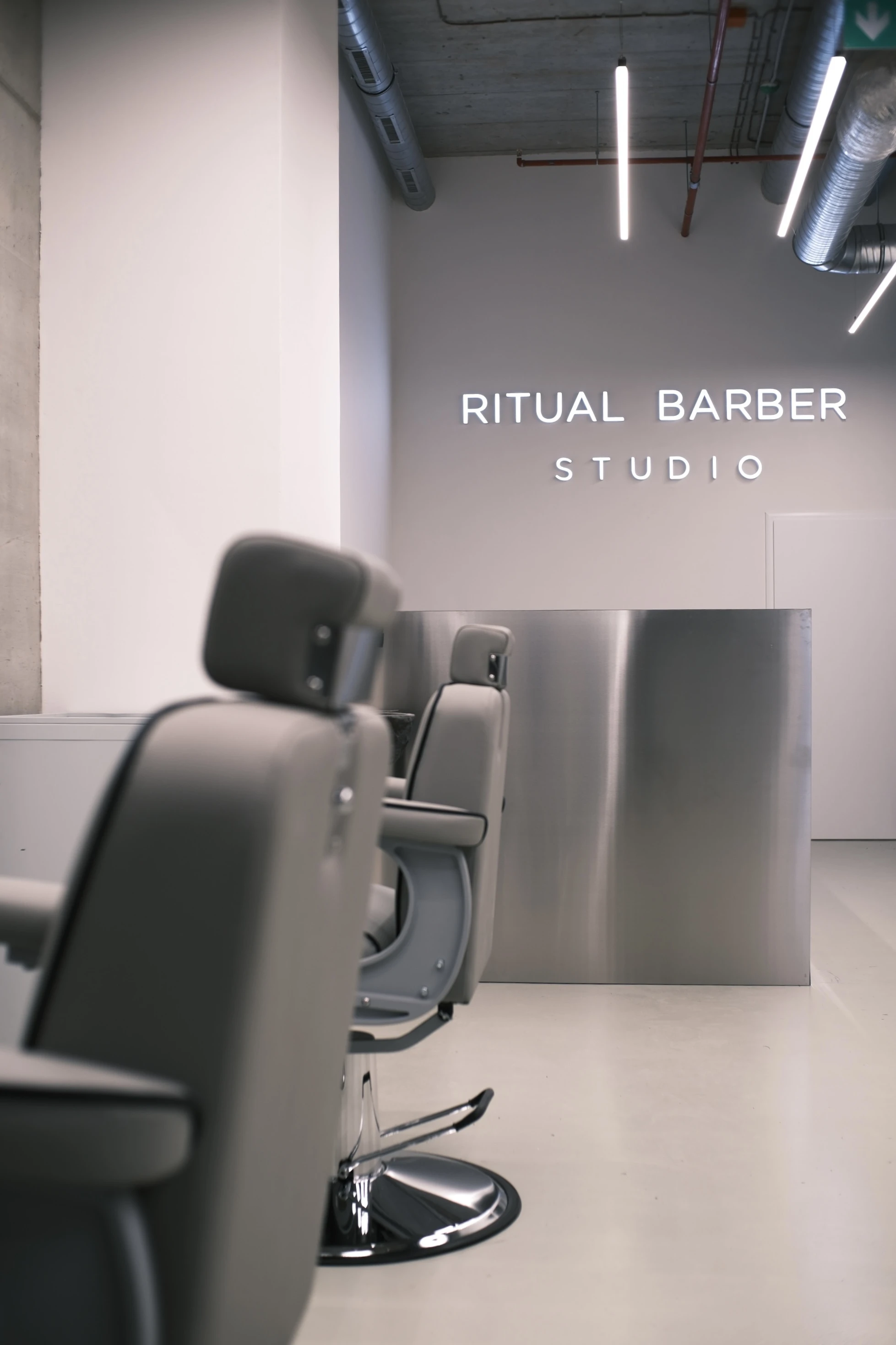 Podsvícený nápis Ritual Barber Studio nad recepcí, v popředí barberské křeslo